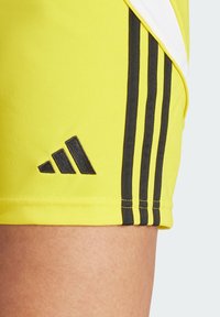 Gelbe Sportshorts mit schwarzen Streifen, ausgestattet mit einem schwarzen Adidas-Logo am Saum. Glatte Textur und atmungsaktives Stoffdesign.