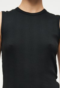 Μαύρο αμάνικο πλεκτό τοπ με ριμπ ύφανση και στρογγυλή λαιμόκοψη, φορεμένο από άτομο που φαίνεται από τον λαιμό μέχρι τη μέση.