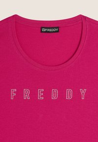 Camiseta de cuello redondo fucsia con mangas cortas, que presenta la palabra "FREDDY" en letras plateadas en la parte delantera. Fabricada con un tejido suave y ligero.
