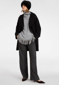 Zwarte jas met gouden knopen, grijze coltrui met franjes, grijze broek met wijdbenen en een zwarte bonten hoed. Bruine puntige ballerina's maken de look compleet.