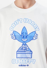 Balts kokvilnas T-krekls ar zilu grafisko tekstu "NELIELIETIETIES - ESIET PRIEKŠ" un smaidīgu tēlu ar adidas zīmola apaviem un akcentiem.