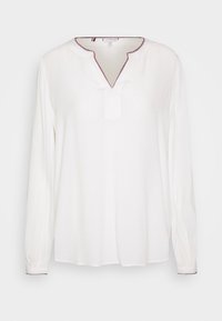 Blusa bianca a maniche lunghe con scollo a V e un piccolo taglio, decorata da cuciture rosse lungo il colletto e i polsini. Tessuto morbido.