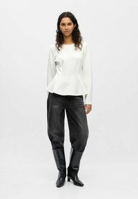 Haut peplum blanc à manches longues, associé à un jean noir ample et des bottes noires texturées jusqu'aux genoux. Design minimaliste et lignes épurées.