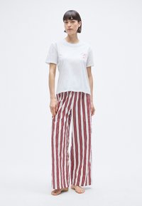 T-shirt en coton blanc avec un petit motif rouge, associé à un pantalon de pyjama à jambes larges présentant des rayures verticales rouges et blanches.