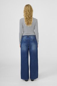 Széles szárú kék farmernadrág, amelynek elhalványult textúrája van, öt zsebes dizájnnal és sötét függőleges csíkos hosszú ujjú pólóval.