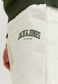 Light gray sweatpants with a textured finish, featuring a dark green logo "JACK & JONES" in an arch style, and a side pocket.