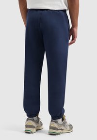 Navyblauwe joggingbroek met elastische tailleband en boorden. Glad, zacht materiaal; casual ontwerp. G dragen met grijze en gele sport sneakers.