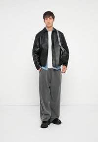 Sort læderjakke, grå oversized bukser, hvid t-shirt, denimskjorte under, og sorte sko med strukturerede såler.