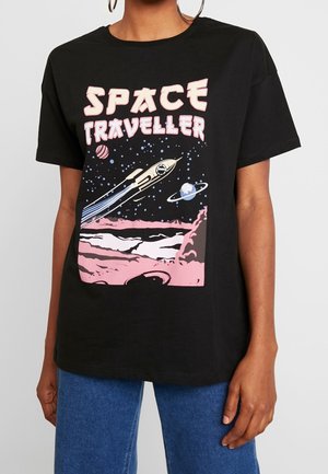 Osoba ubrana w czarną koszulkę z rakietą lecącą w kosmosie, planety, gwiazdy i tekst "Space Traveller" w kolorze różowym i białym.