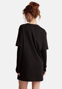 Czarna, oversize sukienka t-shirtowa z krótkim rękawem, cechująca się luźnym krojem i prążkowanymi akcentami długich rękawów na ramionach. Miękka tekstura materiału.