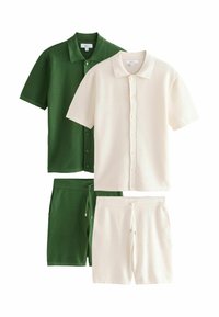 Deux chemises en tricot à manches courtes boutonnées et shorts assortis à cordon de serrage en vert et blanc cassé, posés à plat sur un fond blanc.