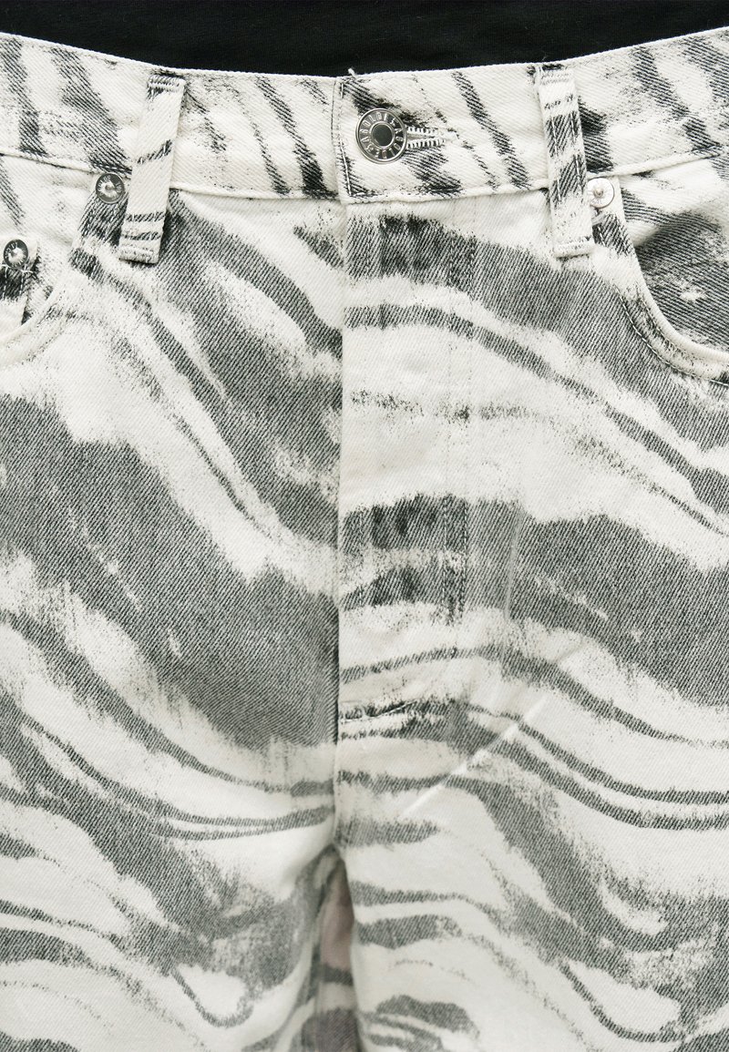 Nahaufnahme von Jeans mit hohem Bund mit schwarz-weißem Zebramuster, Metallknopf, Gürtelschlaufen und sichtbaren vorderen Taschen.