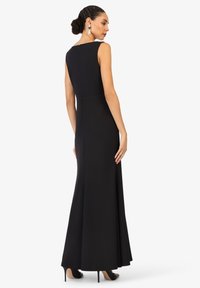 Robe de soirée noire sans manches avec un corps ajusté et une jupe évasée. Présente une fermeture éclair dissimulée au dos et une texture de tissu lisse.