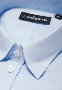 Jasnoniebieska koszula z krótkim rękawem i kołnierzykiem zapinanym na guziki, wykonana z teksturowanej tkaniny. Zawiera białe guziki i czarną metkę z napisem "LANCERTO."