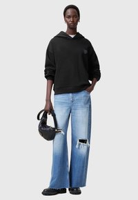 Felpa nera oversize con tasca frontale, abbinata a jeans larghi sbiaditi di un blu chiaro. Una borsa nera e stivali neri con suola spessa completano il look.