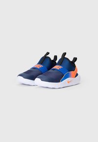 Para granatowych sneakersów typu slip-on od Nike z jasnopomarańczowymi akcentami i białymi podeszwami, z elastycznymi paskami ozdobionymi pomarańczowym logo Nike.
