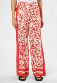 Szerokie spodnie w czerwono-białe wzory z jednolitą czerwoną boczną falbaną i paskowanym wykończeniem; wykonane z lekkiego materiału.