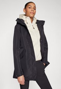 Schwarze wasserdichte Jacke mit Kapuze, ausgestattet mit einem Reißverschluss, vorderen Taschen und einem hellfarbigen Innenfutter mit einem strukturierten Muster.