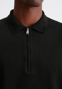 Black long-sleeve polo with a zippered neck. Features a classic collar and soft fabric texture. Zipper hardware is silver.