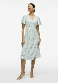 Vestido envolvente floral en azul claro con mangas cortas acampanadas, cintura con lazo y dobladillo a la altura de la rodilla. Presenta pequeños patrones en amarillo y verde.