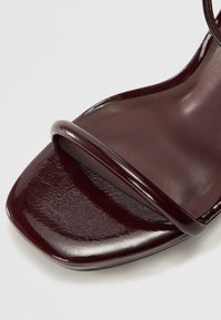Burgundy patent leather sandal with a square toe, featuring a wide strap across the foot and a smooth, glossy surface texture.
