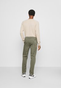 Lichtbeige overhemd met lange mouwen, olijfgroene broek en witte sneakers met zwarte accenten, gezien van de achterkant. Glad textuur en casual pasvorm.