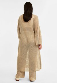Beiger Netz-Kimono mit langen Ärmeln und Seitenschlitzen, mit einer offenen Webstruktur über passenden Hosen. Leicht und locker sitzendes Design.
