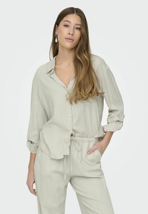 Light gray, long-sleeve button-up shirt with a relaxed fit, featuring a chest pocket, and paired with matching elastic waist pants.
