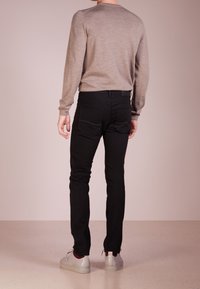 Szary sweter z dzianiny połączony z czarnymi dżinsami. Sneakersy mają teksturowaną powierzchnię i kontrastujące akcenty. Widok z tyłu.