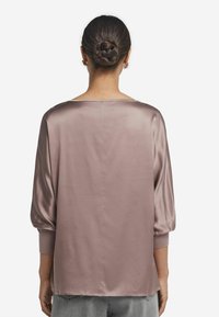 Blusa di raso in malva con una vestibilità rilassata, scollo a barca, maniche a tre quarti e orli cuffiati. Texture liscia con cuciture minime.