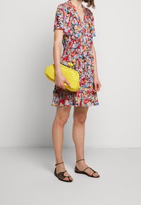 Floral print dress with short sleeves, v-neck, and flared hem. Yellow textured clutch with rounded edges. Black strappy sandals.
