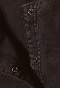 Schwarzer Baumwollstoff mit strukturierter Oberfläche, ausgestattet mit metallischen Druckknöpfen und Nahtdetails entlang der Kante, die ein schlichtes Design präsentieren.