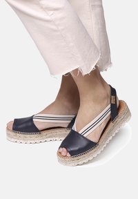 Navy leather espadrille sandals with open toes, featuring striped elastic straps and a woven jute sole with a scalloped edge.