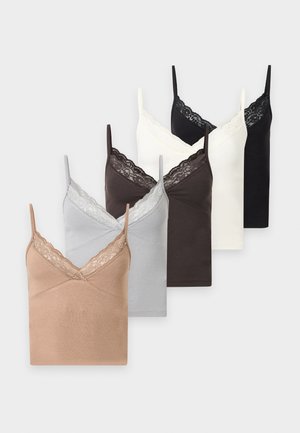 Femme portant un caraco noir, une mini-jupe en jean bicolore et des bottes noires montant jusqu’aux genoux, debout sur fond blanc.