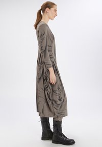 Un largo vestido gris de una tela suave y drapeada, con mangas largas y detalles recogidos; combinado con botas de combate negras.
