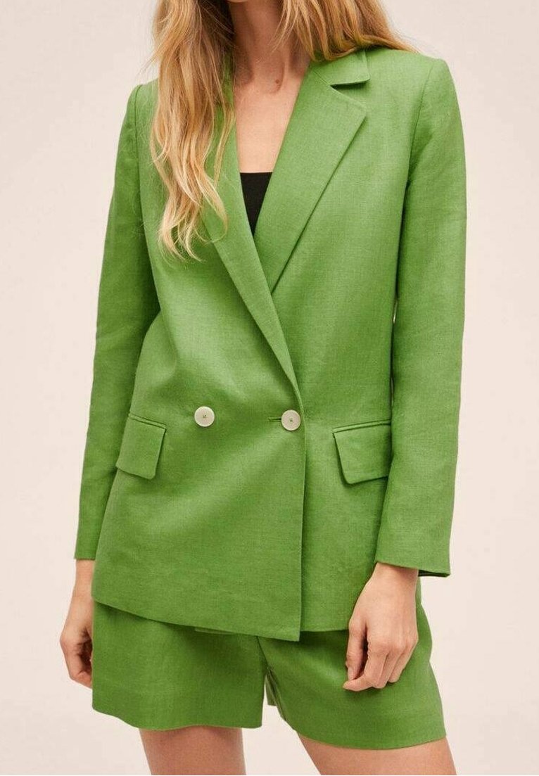 Blazer verde in lino con doppi bottoni, rever a punta e due tasche frontali. Indossato con pantaloni corti coordinati, il tessuto ha una texture liscia.
