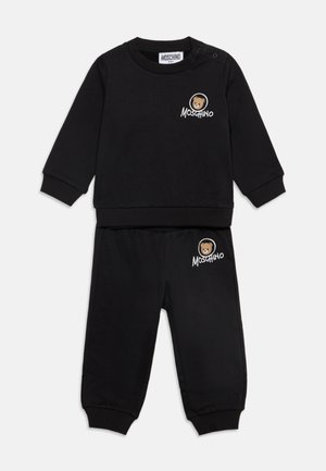 Ensemble bébé noir sweat-shirt et pantalon avec logo ours en peluche et texte Moschino sur la poitrine et la cuisse, poignets et ceinture côtelés.