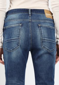 Dunkelblaue Denim-Jeans im mittelhohen Design, mit zwei Gesäßtaschen mit Stickdetails und einem Markenlabel aus Leder am Bund.