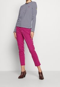 Maglietta a maniche lunghe a righe blu e bianche abbinata a pantaloni rosa slim-fit e stivaletti con tacco marroni. Presenta un logo sulla maglietta.
