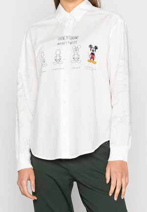 Camisa blanca con botones, con bocetos paso a paso en negro y colores que muestran cómo dibujar a Mickey Mouse en la parte frontal.