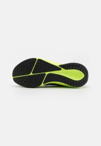 Semelle de chaussure en caoutchouc noir avec un motif de grip texturé et une accentuation en néon vert vif le long du bord. Design léger pour une traction optimale.
