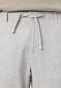 Calças em mistura de linho cinza claro com um acabamento texturizado, cintura com cordão elástico e bolsos laterais, exibindo um design casual.