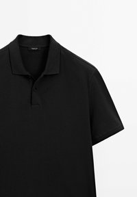 Polo noir à manches courtes avec col et patte de boutonnage à deux boutons, posé à plat sur une surface blanche.