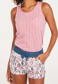 Woman wearing a sleeveless pink patterned tank top and white shorts with multicolor geometric prints and a blue crochet waistband with drawstring.