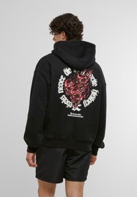 Hoodie negru cu un grafic mare roșu și alb, ce prezintă cranioane și flăcări pe spate. Țesătura pare groasă și texturată.