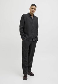 Chemise en lin noire à manches longues avec des boutons sur le devant, associée à un pantalon ample assorti et des chaussures foncées, créant un look monochrome.