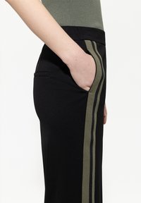 Schwarze Hose mit olivgrünen Seitenstreifen. Sie besitzt einen schlanken Schnitt, ein glattes Material und eine diskrete Seitentasche, die ein modernes Design zur Schau stellt.
