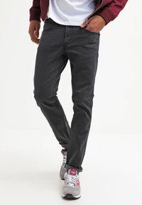 Tummanharmaat farkut slim fit -mallilla, joissa on klassinen viiden taskun muotoilu ja huomaamattomia ompeluyksityiskohtia. Yhdistetty harmaisiin tennareihin.