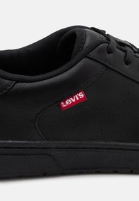 Svarte lær sneakers med teksturert overflate, svarte lisser og rød Levi's-logo på siden. Har perforeringer for ventilasjon.