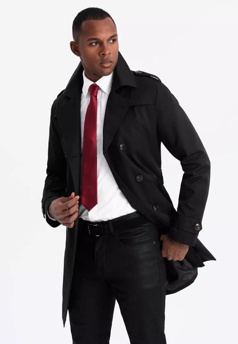 Czarny płaszcz trench z podwójnym zapięciem, szerokim kołnierzem i guzikami. Połączony z białą koszulą i czerwoną krawatem, noszony na czarnych dżinsach.